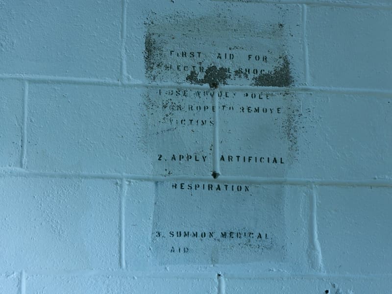 Faded stenciled First Aid for Electrical Shock instructions on a painted wall