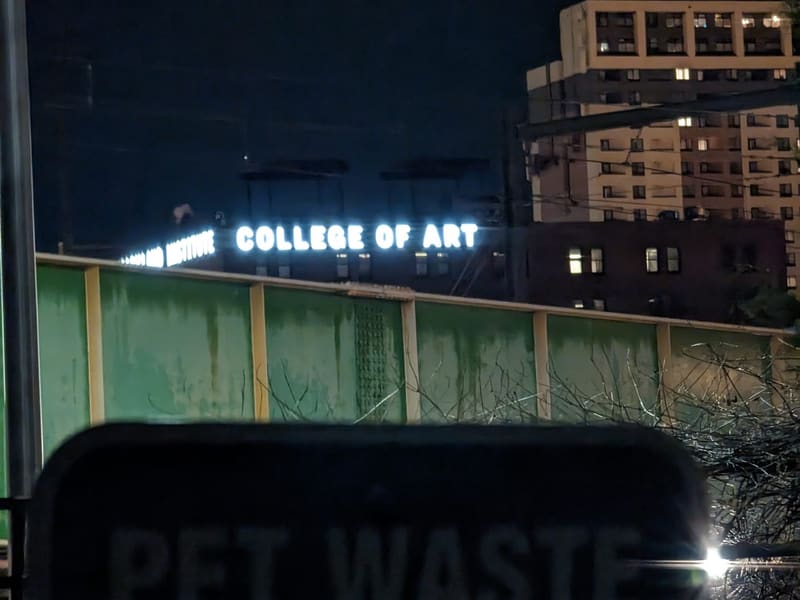 MICA College of Art sign glowing at night above a rail cut