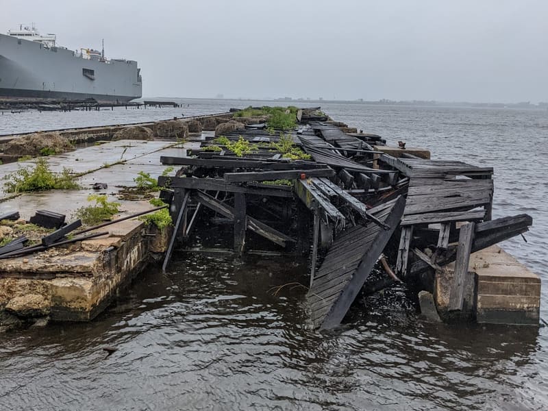 Collapsed wooden pier on the harbor with a cargo ship on a gray day