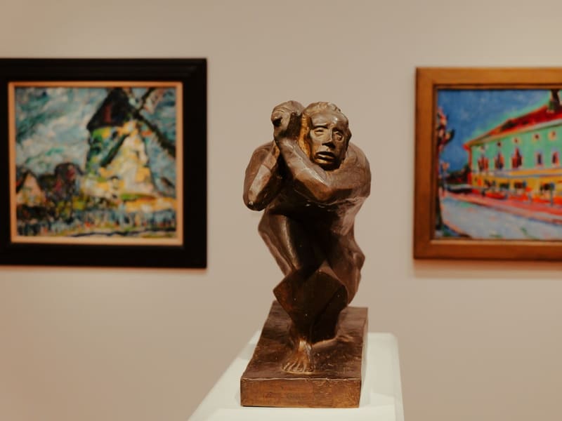 A bronze cubist figure sculpture between two Fauvist paintings