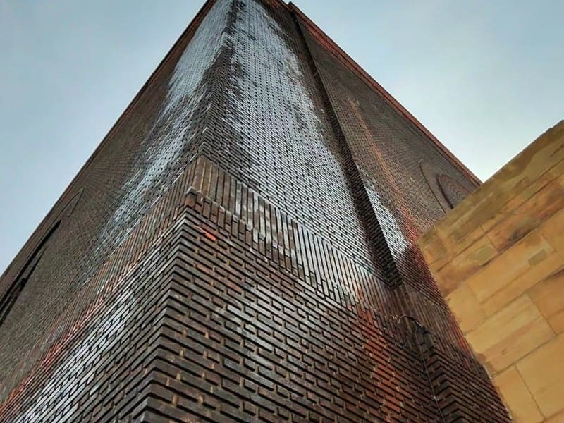 Looking up the rain-streaked brick corner of a tall building against a gray sky