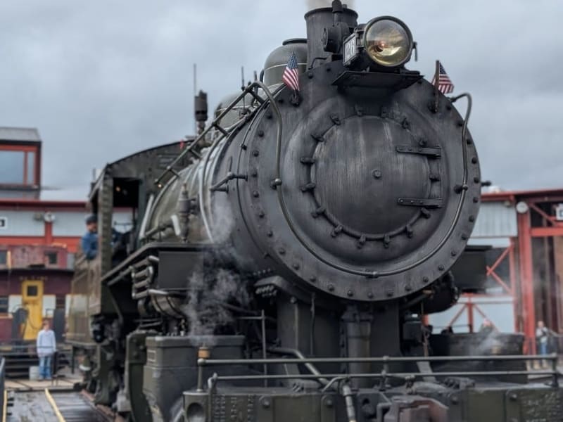 A working steam locomotive venting steam on the turntable, flags on its smokebox