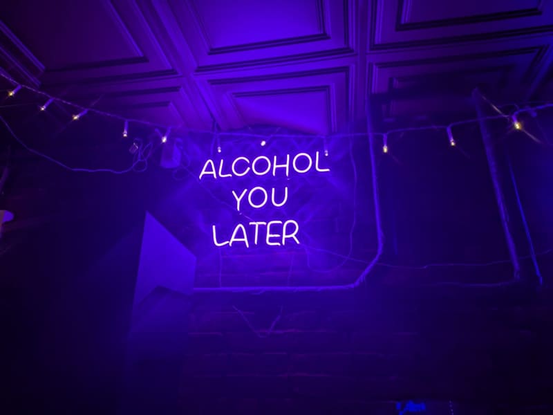 A purple neon bar sign reading 'Alcohol You Later'