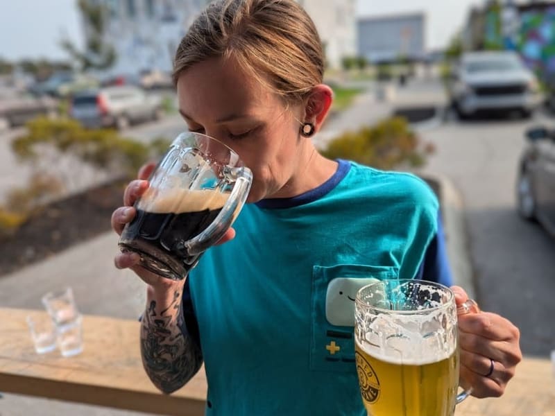 A person sipping a stout while holding a lager on a brewery deck