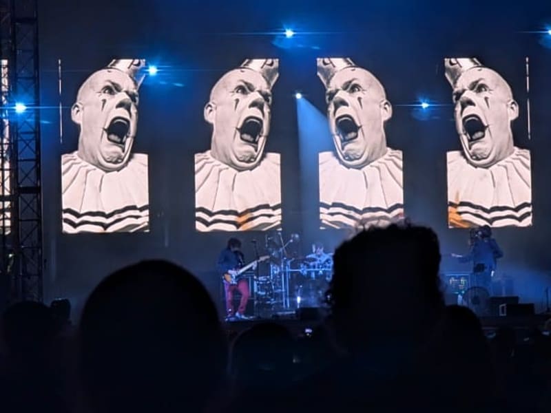 A concert stage washed in blue light with screens of a screaming clown-faced figure