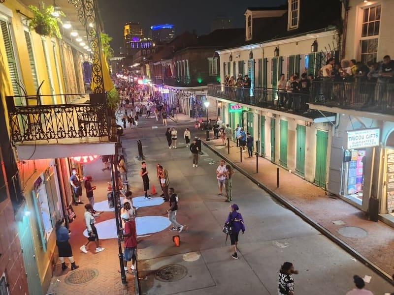 Bourbon Street at night, crowds and balconies below the New Orleans skyline