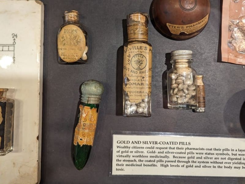 A display case of antique apothecary bottles labeled 'Gold and Silver-Coated Pills' at the Pharmacy Museum