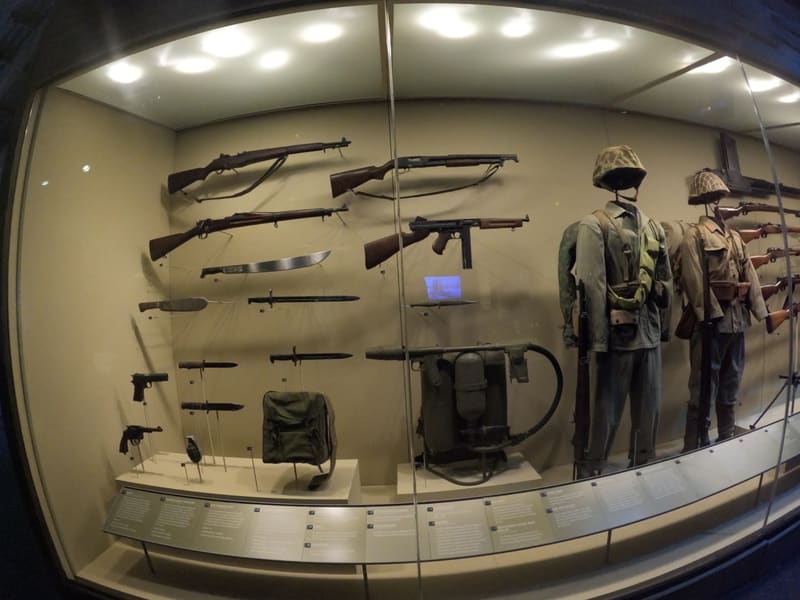 A glass case of WWII rifles, knives and uniformed mannequins at the National WWII Museum