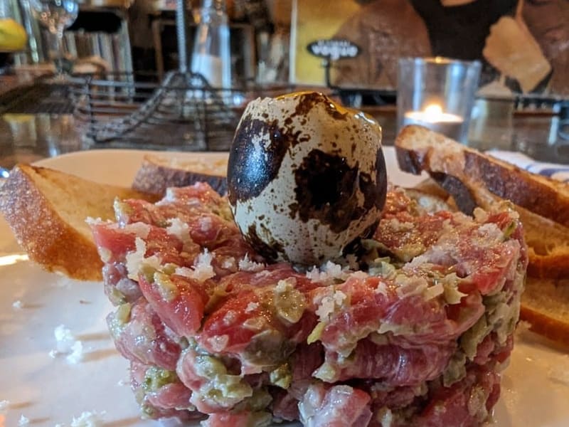 Steak tartare topped with a quail egg, served with toast points