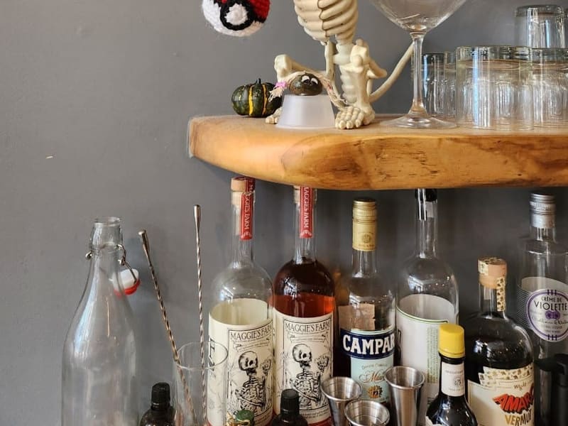 A toy skeleton rat clutching a crocheted Poke Ball on a bar shelf above Maggie's Farm rum