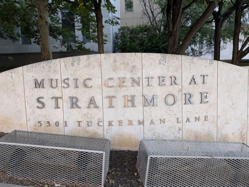 Engraved stone sign reading 'Music Center at Strathmore, 5301 Tuckerman Lane,' framed by trees.