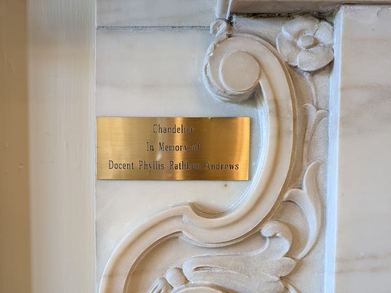 An ornate white plaster scroll carving beside a small brass plaque.