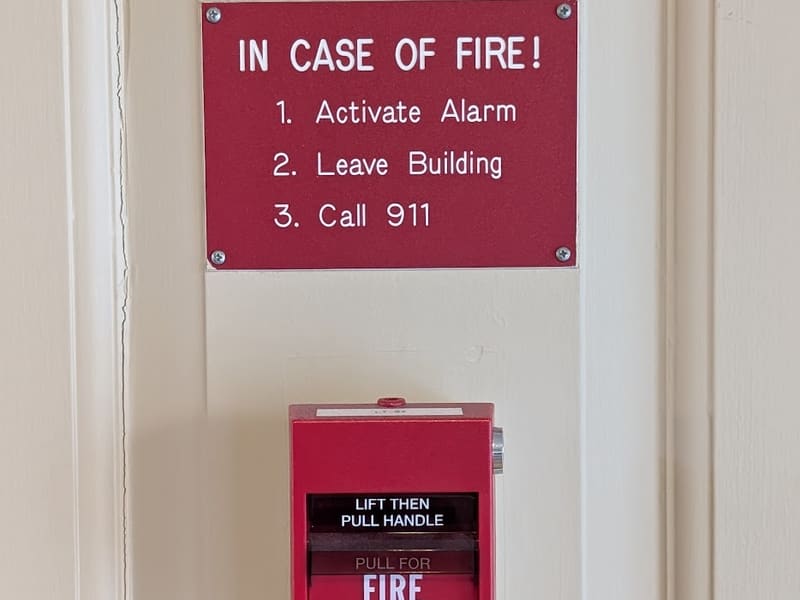 A red 'In Case of Fire' instruction sign mounted above a fire-alarm pull station.