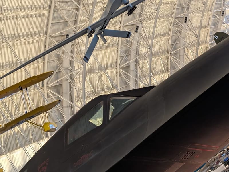The black SR-71 Blackbird cockpit below a suspended Predator drone in the hangar
