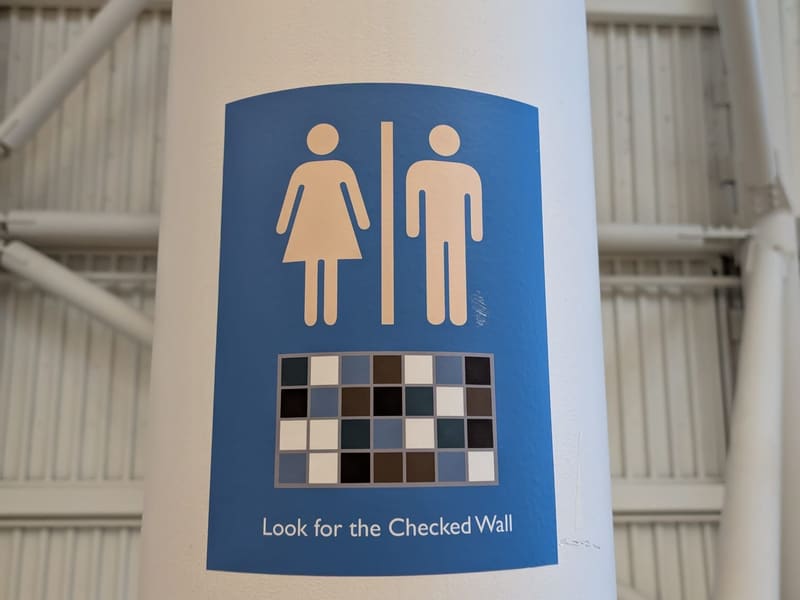 A restroom wayfinding sign reading 'Look for the Checked Wall'