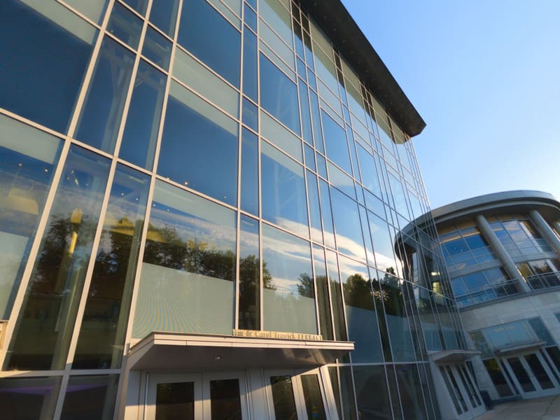Sunlit glass curtain wall of the Music Center at Strathmore, with a rounded glass tower beside the terrace entrance doors.